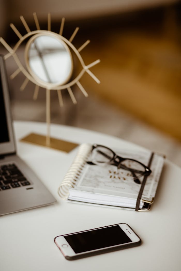 Stylish home office with a laptop, planner, glasses, and phone on a cozy desk.